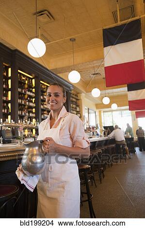 Picture - Hispanic waitress holding pitcher in restaurant. Fotosearch