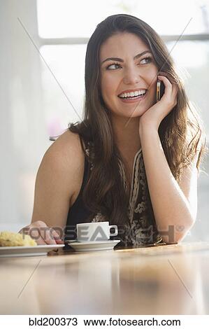 Stock Image - Hispanic woman drinking coffee and talking on cell phone. Fotosearch