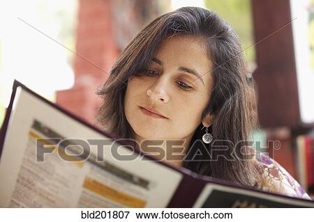 Stock Photo - Hispanic woman looking at restaurant menu. Fotosearch