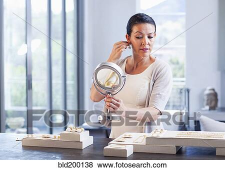 Stock Photo - Hispanic woman trying on earrings in jewelry store. Fotosearch