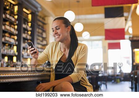 Stock Image - Hispanic woman using cell phone in restaurant bar. Fotosearch