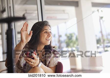 Stock Image - Hispanic woman waving and holding cell phone. Fotosearch