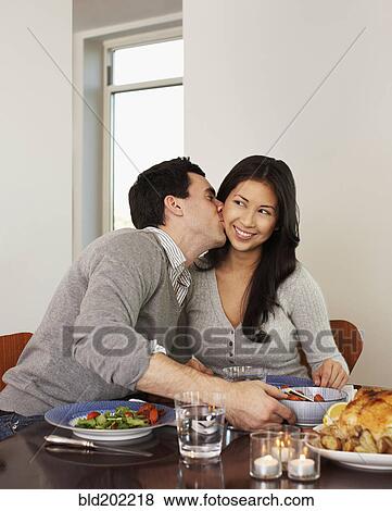 Stock Photo - Husband kissing wife at dinner table. Fotosearch