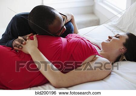 Stock Photograph - Husband laying on bed with pregnant wife. Fotosearch