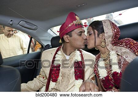 Stock Image - Indian bride and groom in traditional clothing kissing in car. Fotosearch