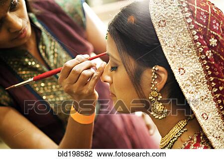 Stock Image - Indian woman in traditional clothing having make up applied. Fotosearch