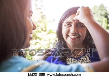 Stock Photo - Indian woman putting jewel on mother's forehead. Fotosearch