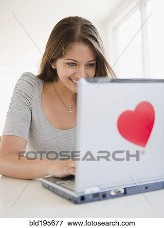 Stock Photo - Indian woman using laptop with heart-shaped sticker. Fotosearch