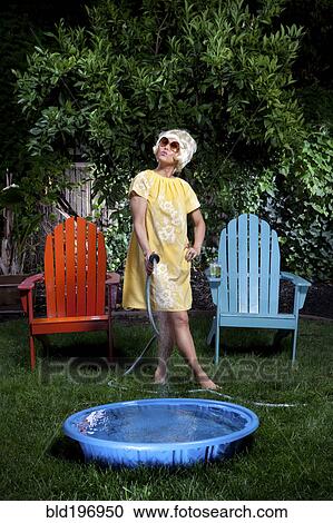 Stock Image - Korean woman filling up small pool in backyard. Fotosearch
