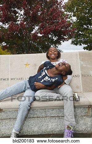 Stock Image - Laughing Black girls sitting on bench. Fotosearch