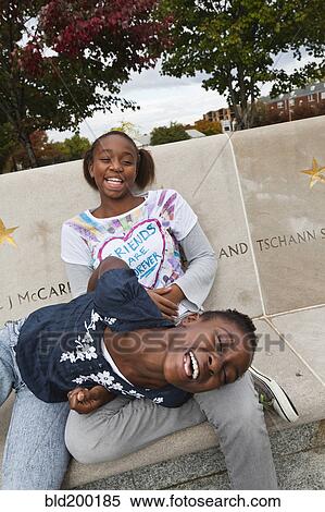 Stock Photography - Laughing Black girls sitting on bench. Fotosearch