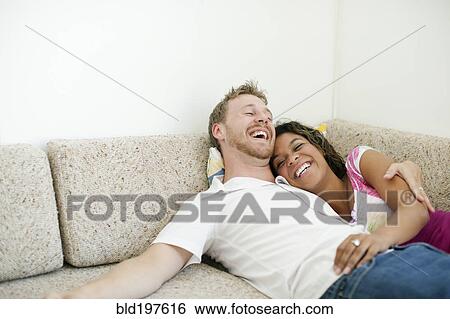 Laughing couple laying on sofa together View Large Photo Image Stock Photograph - Laughing couple laying on sofa together. Fotosearch