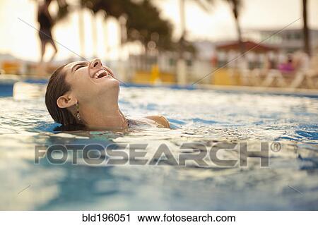 Stock Image - Laughing Hispanic woman swimming in swimming pool. Fotosearch