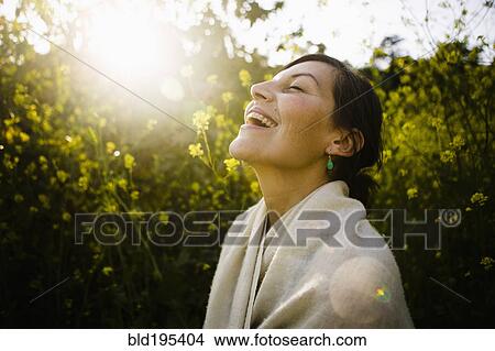 Picture - Laughing mixed race woman with eyes closed in field. Fotosearch