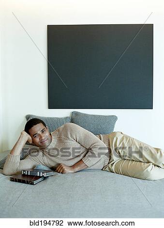 Stock Image - Man laying on bed with books. Fotosearch