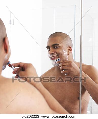Stock Image - Man shaving in bathroom mirror. Fotosearch