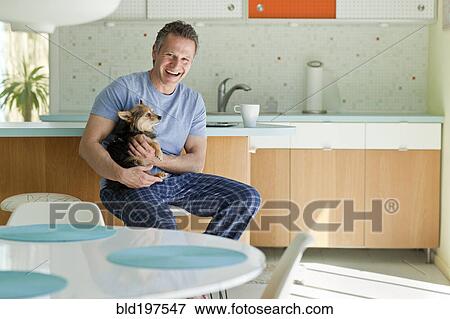 Stock Photo - Man sitting in kitchen with dog. Fotosearch