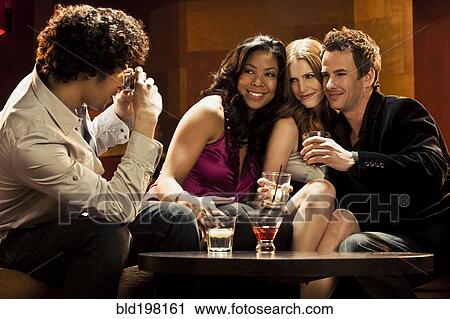 Stock Image - Man taking photograph of friends in nightclub. Fotosearch