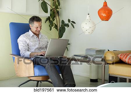 Man typing on laptop in living room View Large Photo Image Stock Image - Man typing on laptop in living room. Fotosearch