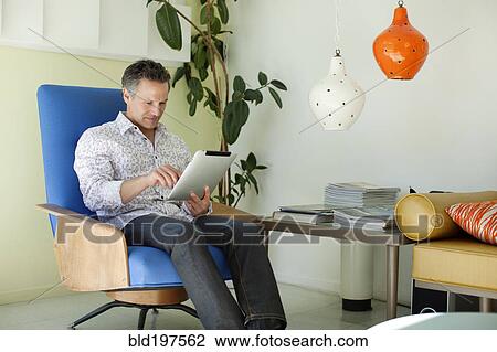 Stock Image - Man using digital tablet in living room. Fotosearch