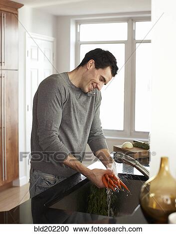 Stock Image - Man washing carrots and talking on telephone. Fotosearch