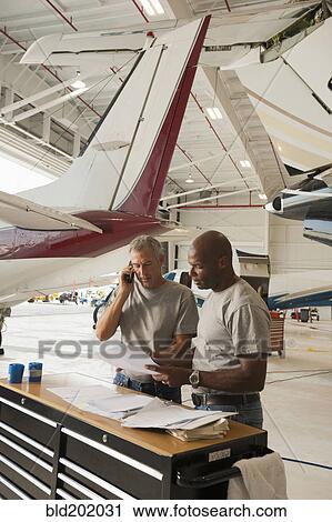 Stock Image - Men working in airplane hangar. Fotosearch