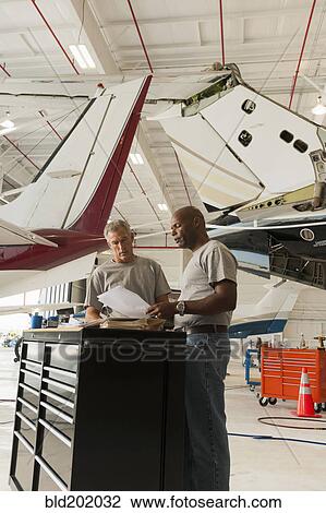 Stock Image - Men working in airplane hangar. Fotosearch