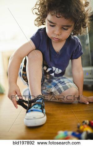 Stock Image - Mixed race boy fastening shoes. Fotosearch