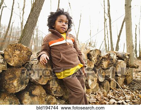 Picture - Mixed race boy leaning against firewood. Fotosearch