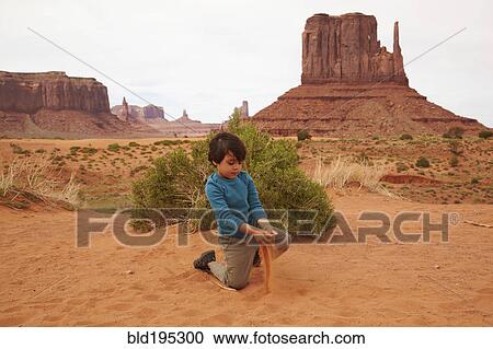 Stock Image - Mixed race boy playing in dirt in Monument Valley. Fotosearch