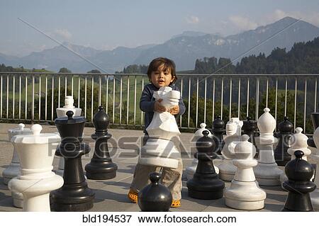 Stock Photo - Mixed race boy playing with large chess pieces. Fotosearch