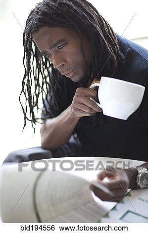 Stock Photograph - Mixed race businessman drinking coffee and reviewing report. Fotosearch