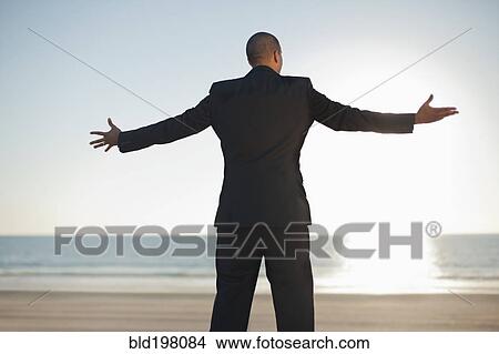 Mixed race businessman standing on beach with arms outstretched View Large Photo Image Picture - Mixed race businessman standing on beach with arms outstretched. Fotosearch