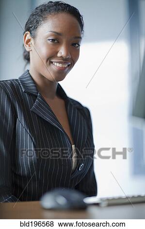 Stock Photo - Mixed race businesswoman sitting at desk. Fotosearch