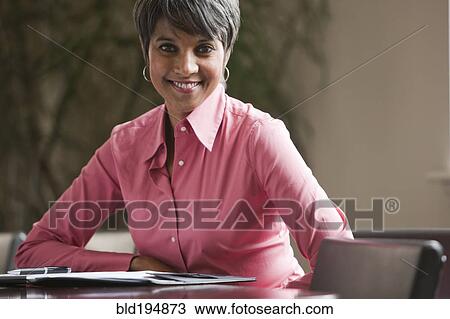 Stock Image - Mixed race businesswoman sitting at table. Fotosearch