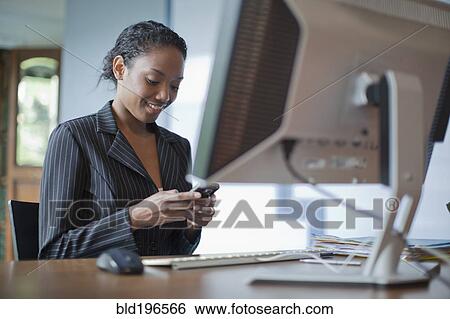 Stock Photograph - Mixed race businesswoman using cell phone at desk. Fotosearch