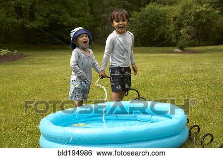 Stock Photograph - Mixed race children filling inflatable pool. Fotosearch