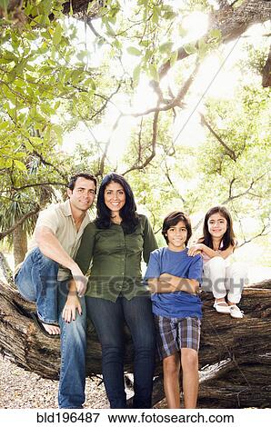 Stock Photo - Mixed race family sitting on large tree branch. Fotosearch