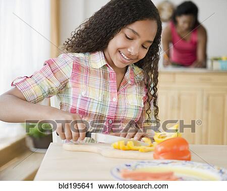 Stock Image - Mixed race girl cutting bell peppers. Fotosearch