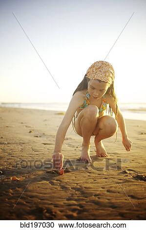 Stock Image - Mixed race girl digging in sand on beach. Fotosearch