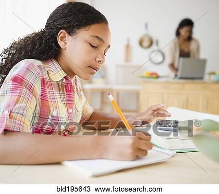 Stock Image - Mixed race girl doing homework in kitchen. Fotosearch