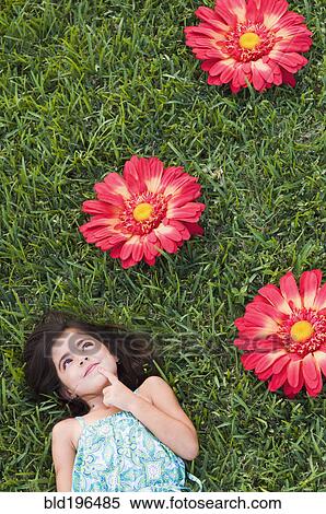 Stock Photography - Mixed race girl laying in grass next to large flowers. Fotosearch