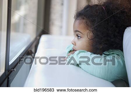 Stock Image - Mixed race girl looking out window. Fotosearch