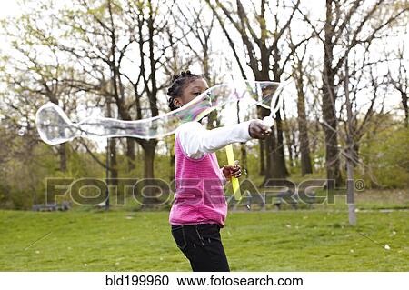 Stock Image - Mixed race girl making bubbles in park. Fotosearch