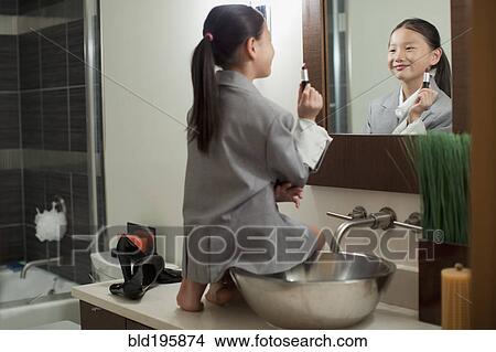 Picture - Mixed race girl on counter putting on lipstick. Fotosearch