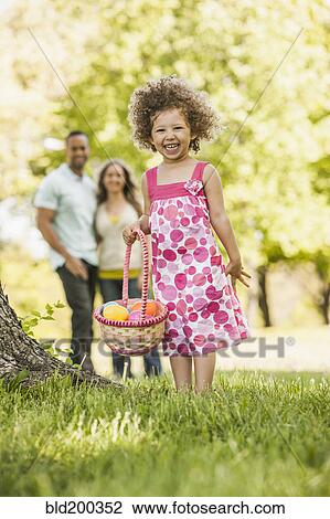Stock Image - Mixed race girl on Easter egg hunt. Fotosearch