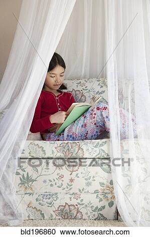 Stock Image - Mixed race girl reading on sofa. Fotosearch