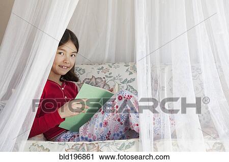 Stock Image - Mixed race girl reading on sofa. Fotosearch