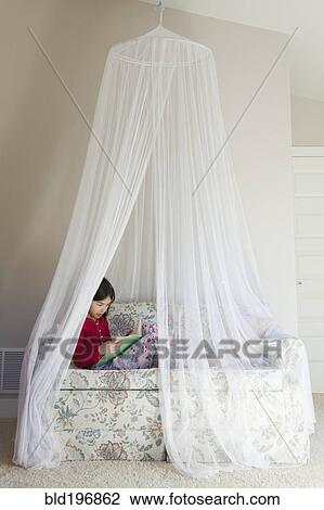Stock Image - Mixed race girl reading on sofa. Fotosearch