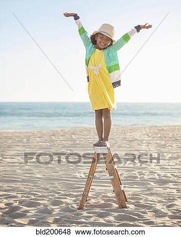 Stock Photo - Mixed race girl standing on ladder on beach. Fotosearch